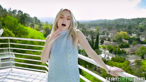 River Fox in light blue turtleneck, teasing with blue eyes on balcony