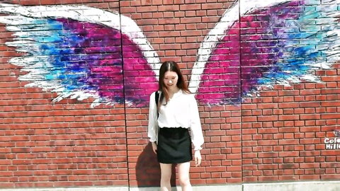 Miu Miu poses teasingly in white blouse and black skirt before colorful wing wall