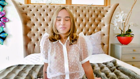 Dakota Tyler in sheer white blouse, seductive seated pose on bed