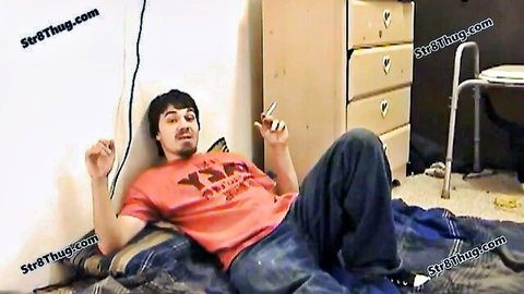 Skinny bearded twink lying on messy floor with jeans down exposing thick hard cock while smoking cigarette