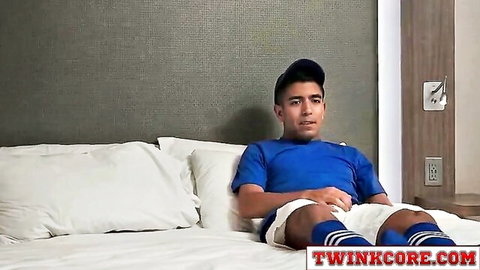 Latin twink in blue sports shirt and shorts sits on bed, awaiting coach's deep anal action