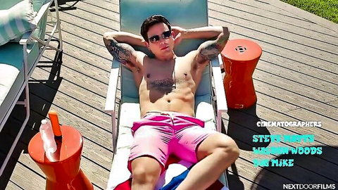 Tattooed shirtless hunk lounging in tight pink swim trunks poolside