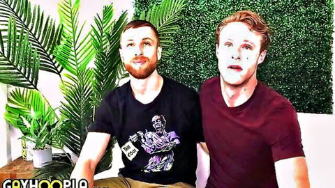 Two muscular gay hunks, bearded stud in zombie tee and freckled guy with white skull face paint, smiling together.