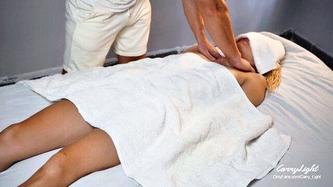 Masseur rubs blonde woman's bare back sensually while she lies nude under towel
