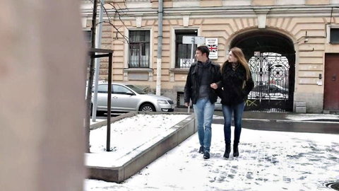 Young brunette woman walks arm-in-arm with man in snowy urban street
