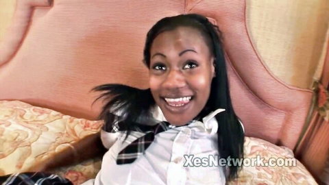 Smiling ebony college girl in school uniform on bed