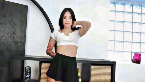 Tattooed Latina babe in white crop top, black mini skirt and fishnets posing seductively