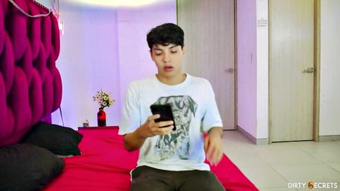 Young Asian guy in t-shirt on bed, surprised with phone, stepbrother blind date threesome