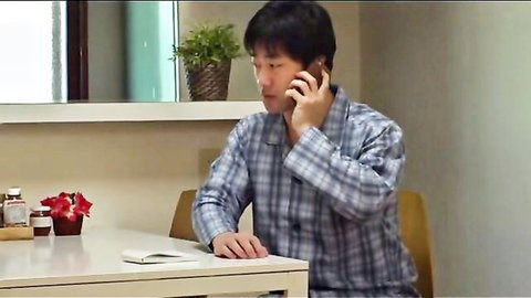 Asian man in plaid pajamas talking on phone at table, casual home scene