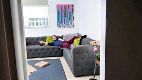 Adria Rae lounges casually on couch in blue top and pants, pizza box nearby