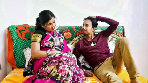Indian couple smiling intimately on bed, wife in pink saree and husband in shirt teasing playfully