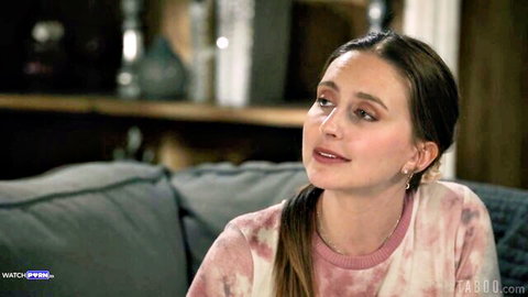 Brunette woman with ponytail in pink tie-dye sweatshirt sitting on couch smiling