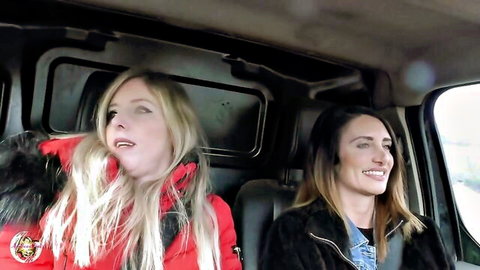 Blonde MILF in red jacket and brunette friend smiling in van, ecstatic faces hinting at wild kink