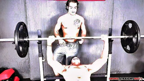 Tanner Valentino shirtless bench pressing with muscular spotter in gym
