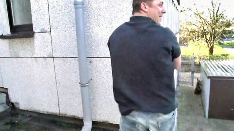 Mature man in casual polo and jeans stands outdoors near building, teasing kinky bath and cum encounter