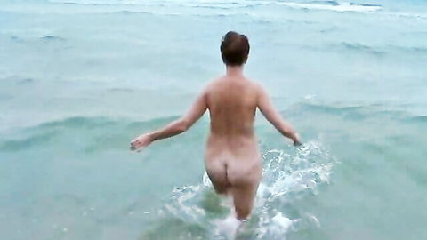 Nude babe with perfect round ass wading into splashing ocean waves from behind
