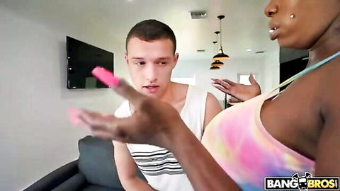 Busty black stepmom in colorful bikini top holds pink dildo while gesturing at shocked stepson on couch