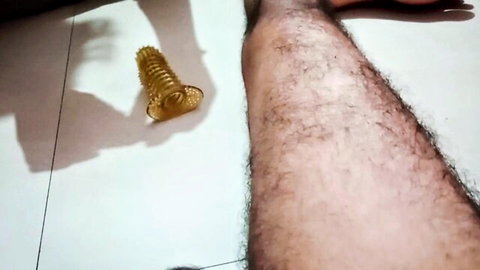Hairy man's leg beside large yellow ribbed cock dildo on white tiled floor