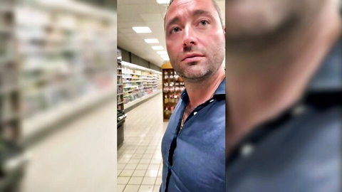 Mature man in open blue shirt smirking in supermarket aisle, teasing public exposure