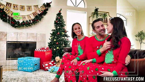 Smiling Latina stepmom and stepsis in tight red Christmas PJs cozy up to lucky stepbro on couch by tree