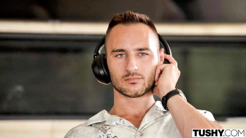 Handsome man adjusts black headphones over ears wearing patterned shirt in studio