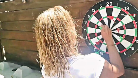 Blonde woman with wet hair in tight white tank top throwing dart at board from behind