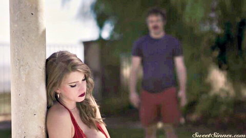 Octavia Red in red slip dress leaning on pillar, man lurking behind