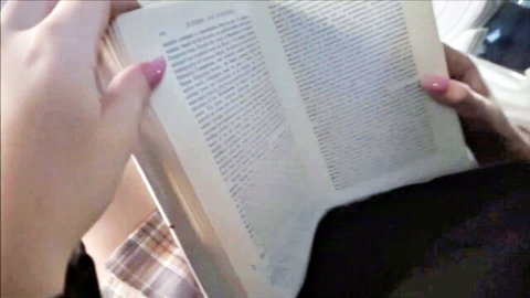 Feminine hands with pink nails holding open book pages, plaid skirt hem visible