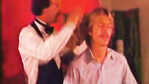 Vintage gay scene: waiter grooming long-haired blond man