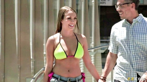 Busty brunette in skimpy yellow bikini top and jeans walks hand-in-hand with older man outdoors