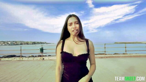 Curvy teen with big tits in low-cut black dress showing deep cleavage outdoors on sea promenade