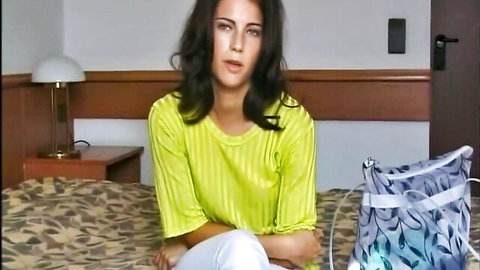 Viktoria in Pierre Woodman's casting, sitting on bed in yellow top and white pants