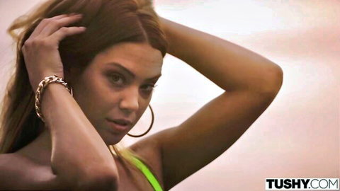Seductive long-haired brunette teasing with hands in hair wearing neon green micro bikini top