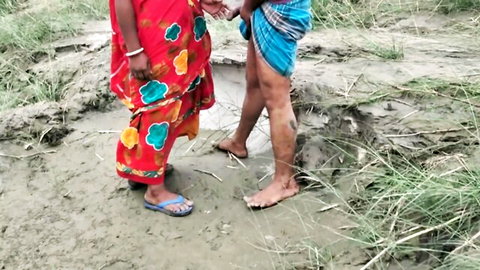 Indian MILF in red floral saree touching man's dhoti bulge outdoors in muddy field