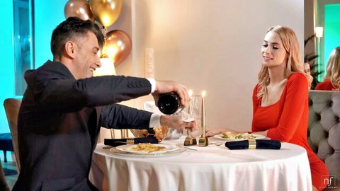 Hot blonde in tight red dress smiles at suited man pouring red wine during romantic candlelit dinner