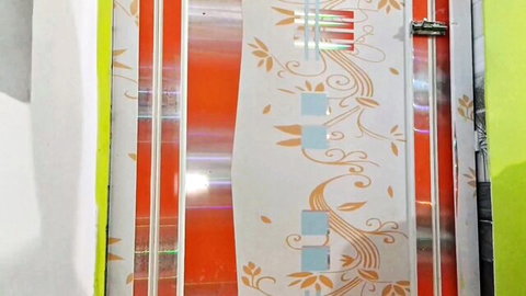 Ornate orange floral patterned metal door with green frame and shiny reflections