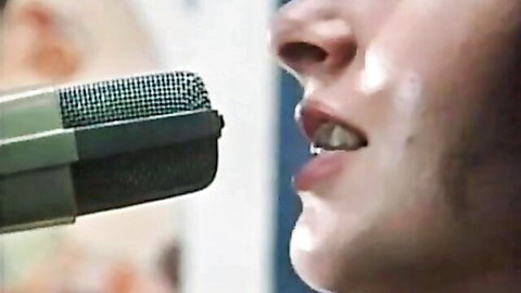 Close-up of woman's open mouth sucking vintage microphone like cock in retro tease.