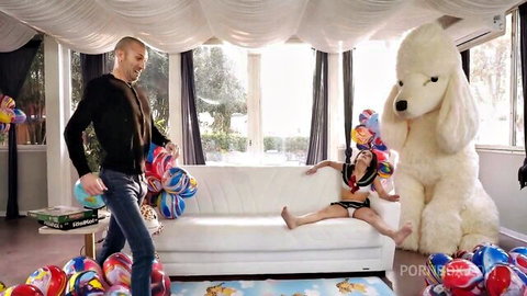 Petite bikini babe spreads legs wide on couch with giant poodle plush and balloons as bald guy approaches