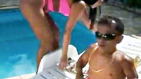 Curvy Latina in pink bikini poses with short muscular guy in red trunks by pool