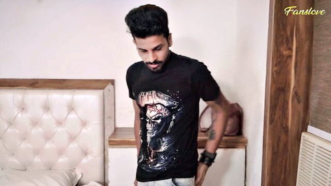 Handsome bearded Indian man in skull t-shirt posing casually by bedroom bed