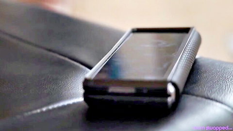 Black foldable phone resting on dark leather couch with wife swapped watermark