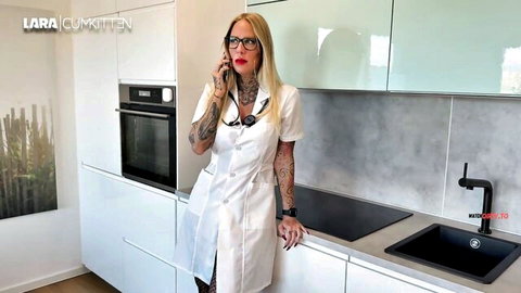 Blonde tattooed nurse in short white lab coat and pantyhose posing sexy on phone in kitchen
