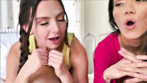 Young Latina teen in yellow tank top moans with open mouth beside Asian babe in pink top gesturing in ecstasy