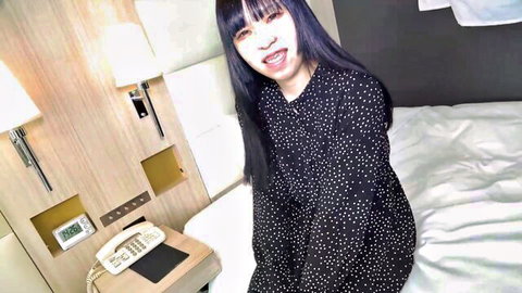 Smiling Asian woman in black polka dot dress on bed, teasing for VR cum-sharing game