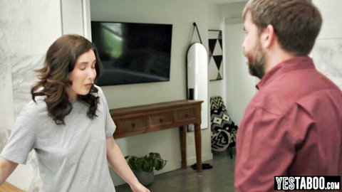 Brunette housewife in gray tank top gestures to bearded husband in living room home setting