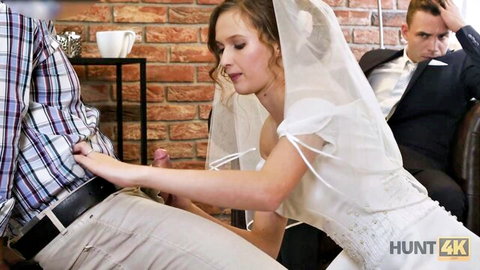 Blonde bride in veil and white dress strokes groom's cock while groomsman watches