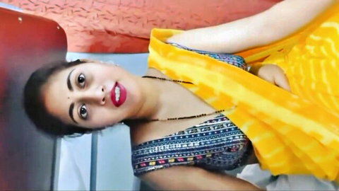 Sexy Indian woman in yellow saree blouse teasing deep cleavage with pouty red lips selfie