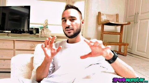 Bearded Arab man gesturing with open hands on couch in white tee solo tease