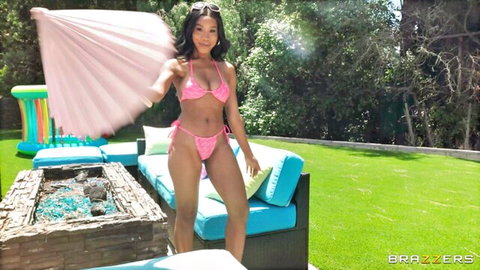 Ebony babe in skimpy pink bikini twirling fan by pool teasing curves and tits