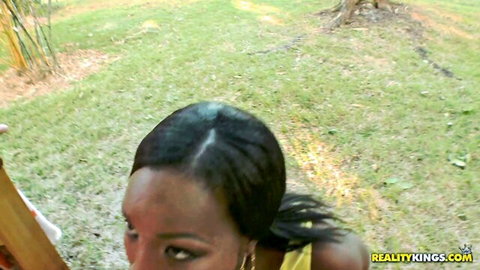 Sweaty ebony woman with ponytail stares intensely outdoors on grass in yellow top